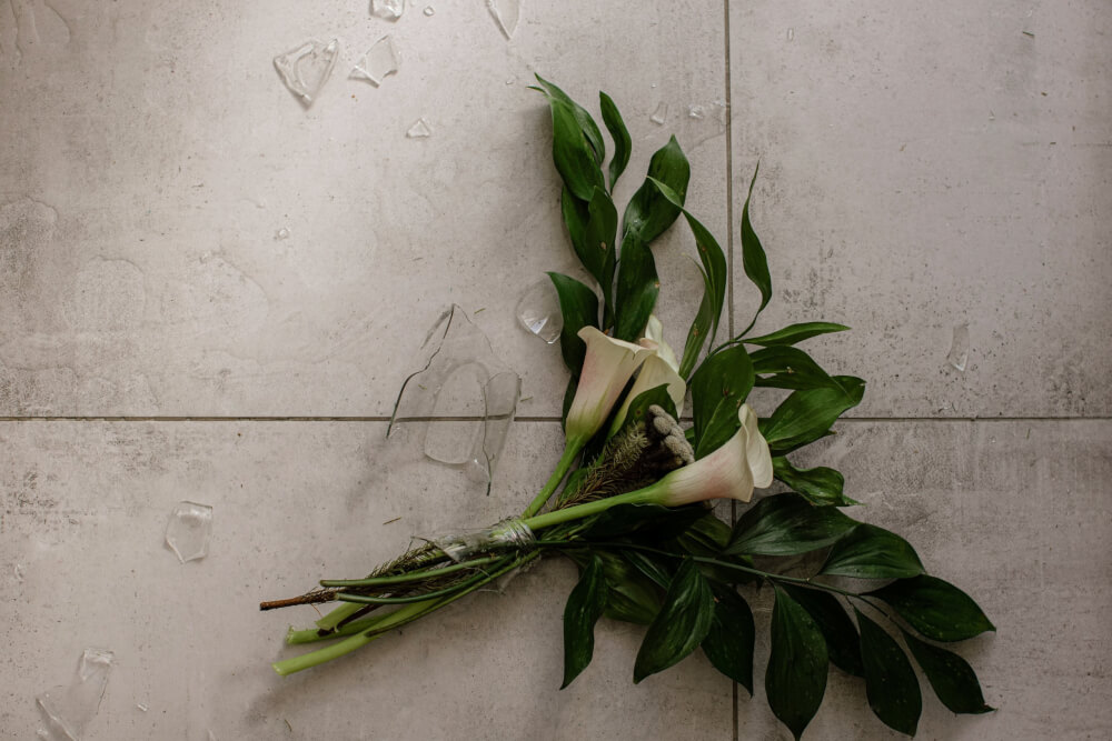 Broken glass vase of flowers on tile floor