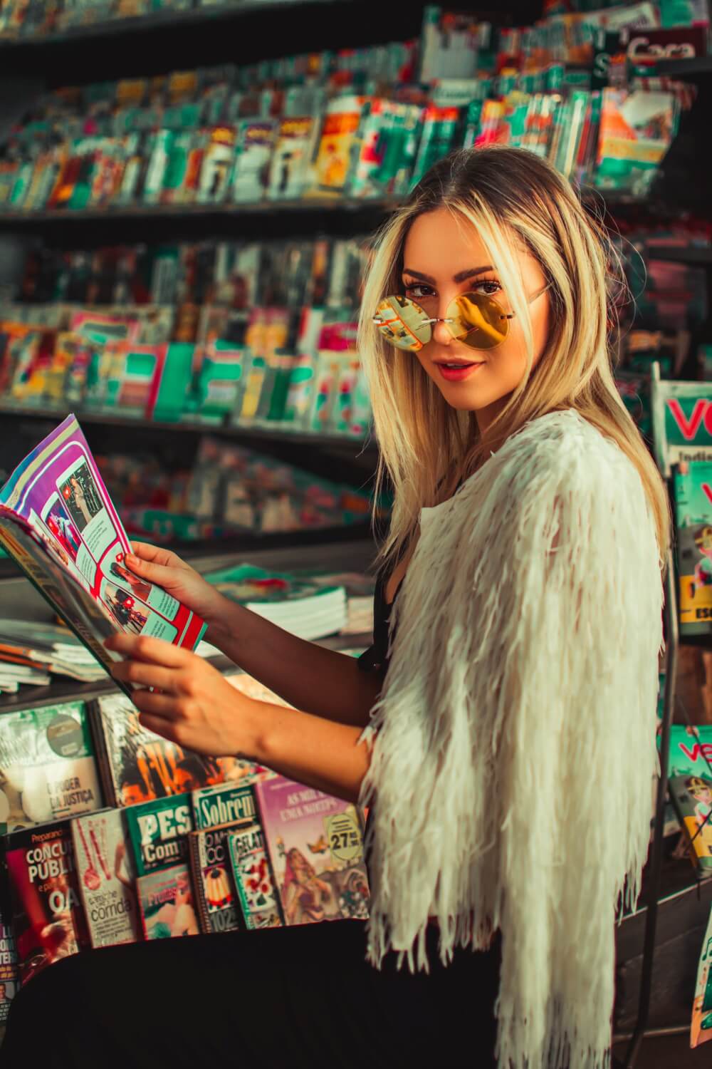 Woman wearing white coat while standing in magazine aisle holding magazine