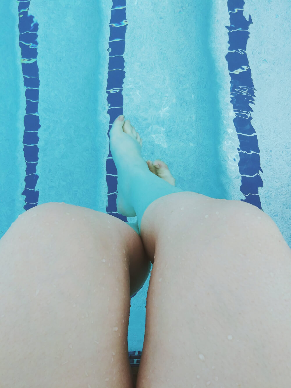 Caucasion thighs outside pool; feet inside pool