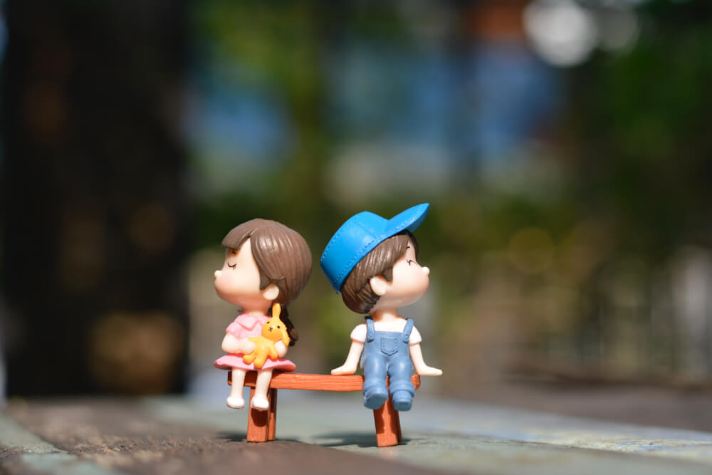 Figurine of girl and boy sitting on bench, looking opposite each other