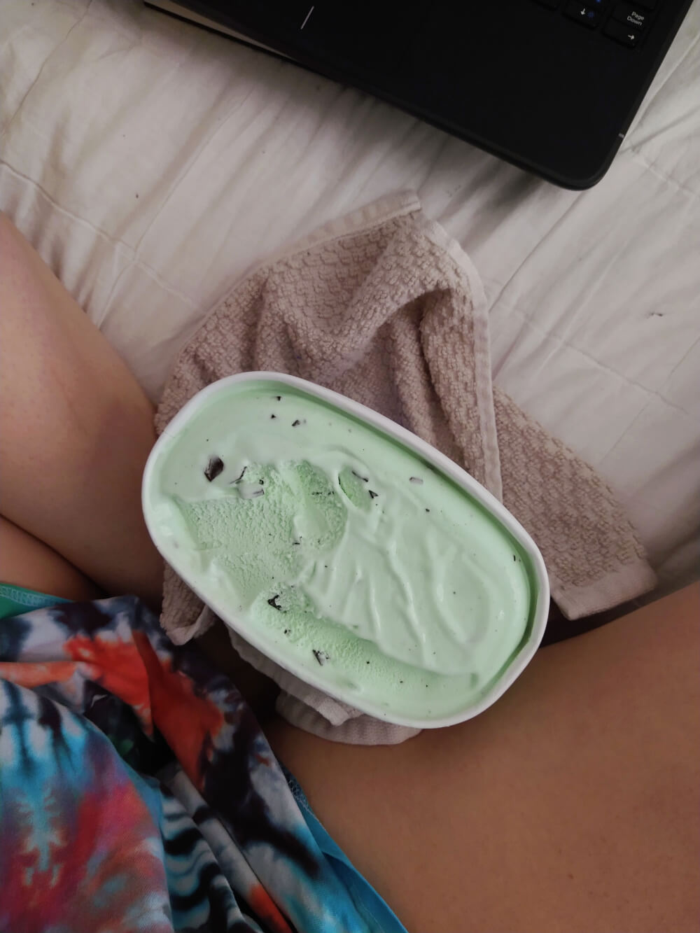 Sitting on bed with mint chocolate chip ice cream in lap (faceless, aerial view)