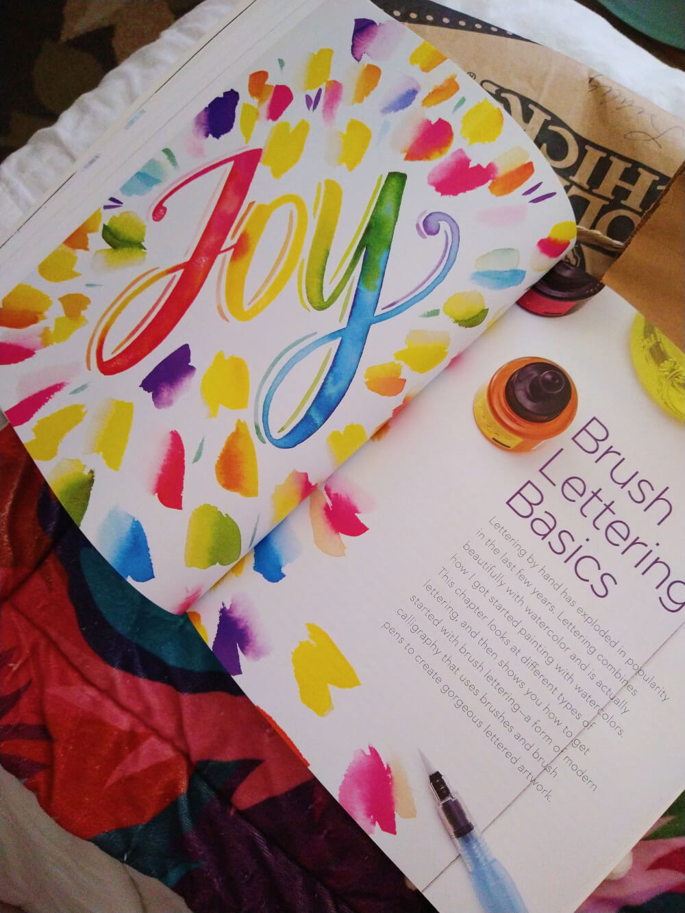 watercolor book open to brush lettering basics, says JOY in watercolor