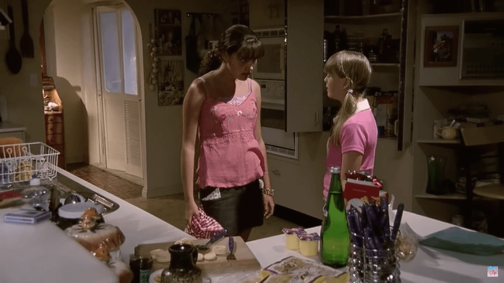 Cleo confronting Kim in the kitchen. They're both wearing pink tops.