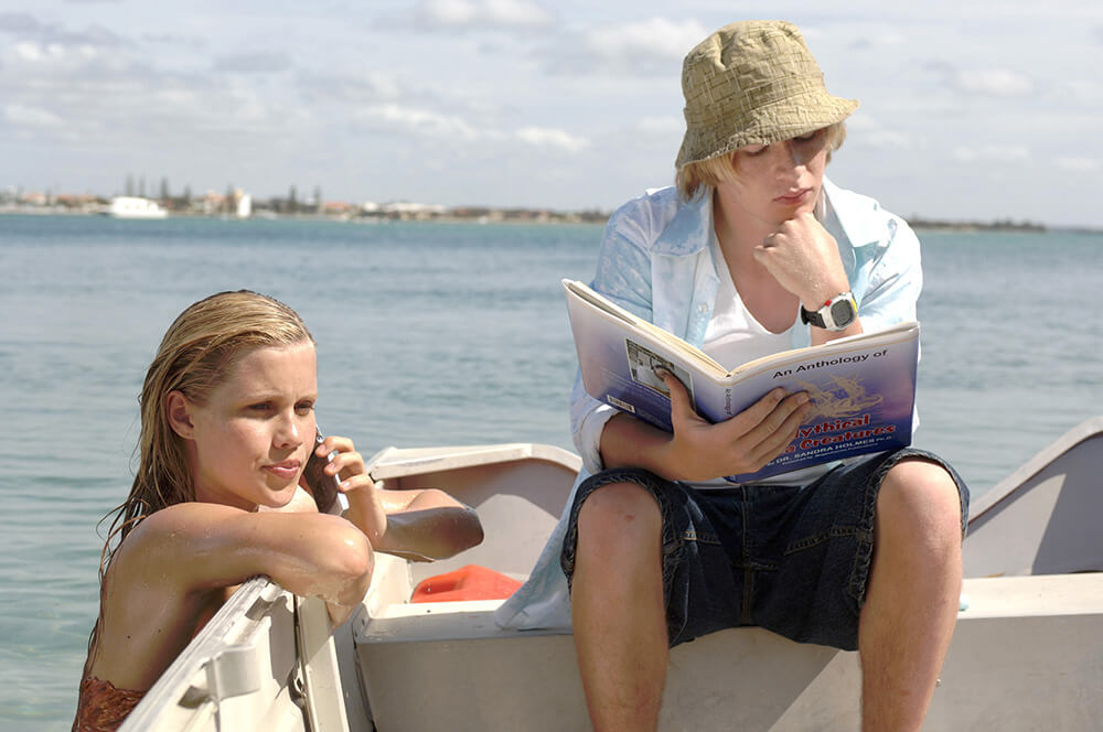 Emma talks to Cleo through the phone while hanging on the side of Lewis's boat, while Lewis reads his book on a bench in the boat