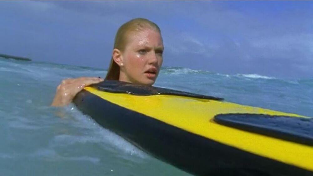 Rikki holding the yellow and black surfboard in the ocean