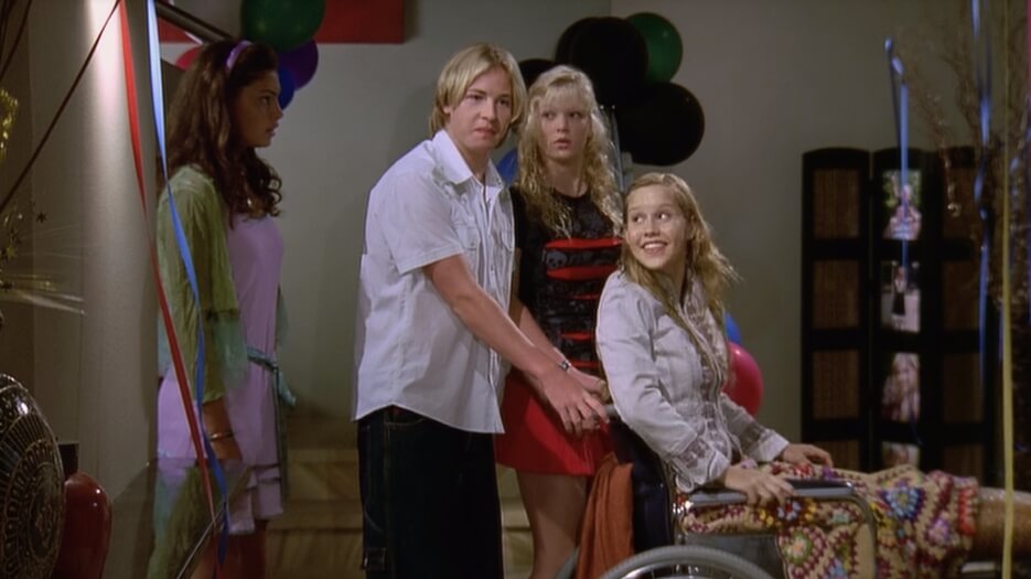 Rikki and Lewis pushing Emma in a wheelchair, with Cleo walking behind them