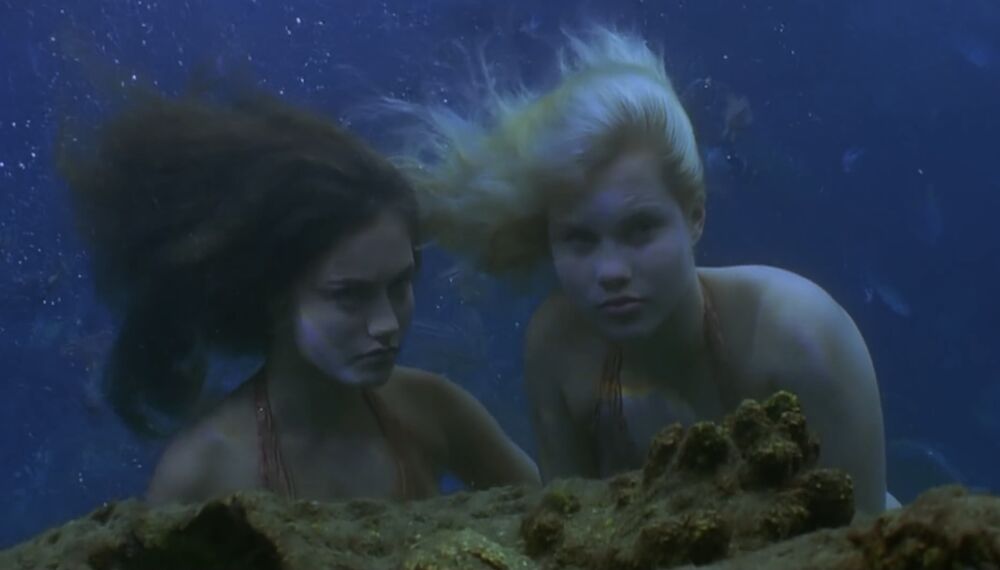 Cleo and Emma underwater, as mermaids, behind a reef