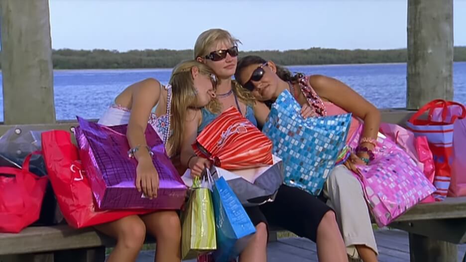 Emma and Cleo lean on Rikki, while they all sit on a bench with their shopping bags
