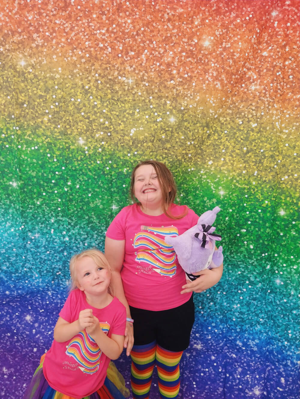 Iah + Fionna in front of a faux glitter rainbow backdrop