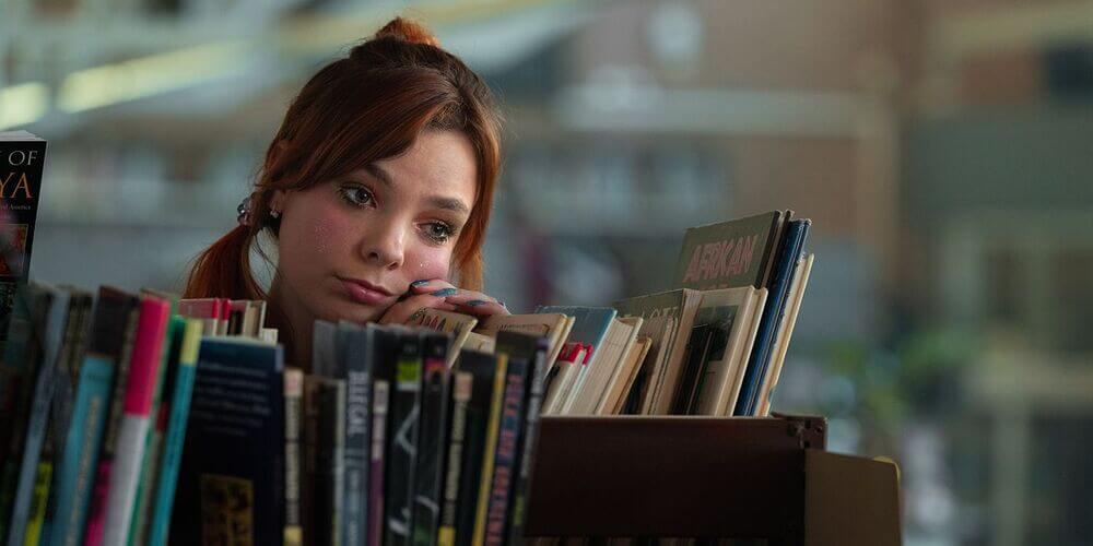 Quinn looking content, resting her head on her hands, resting her hands on a row of books at the library
