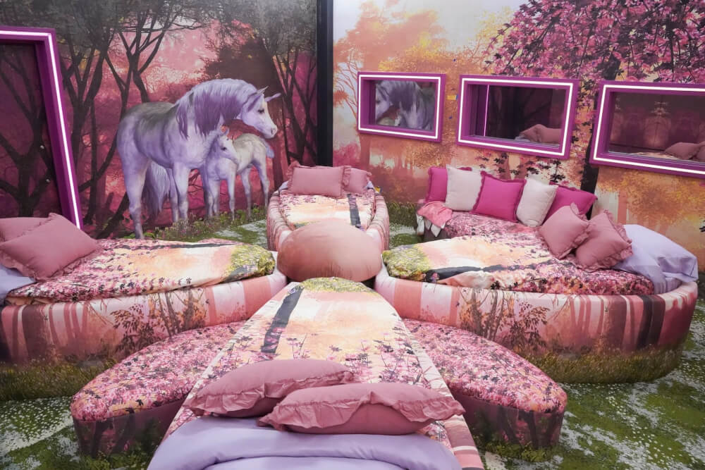 Pink beds arranged like a flower, with a grassy area, two mirrors on a wall instead of windows, and a mural of a unicorn with a smaller unicorn on the wall